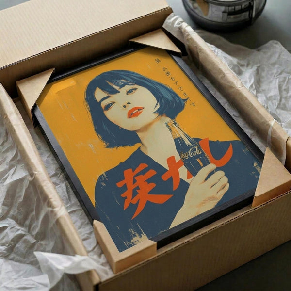 May include: Framed vintage-style Japanese Coca-Cola poster being unboxed from cardboard shipping package with protective wrapping. The retro illustration features a woman with dark bob haircut and red lips holding a Coca-Cola bottle against yellow background, with Japanese characters visible. The black-framed artwork sits nestled in brown cardboard with white tissue paper padding on a light surface.