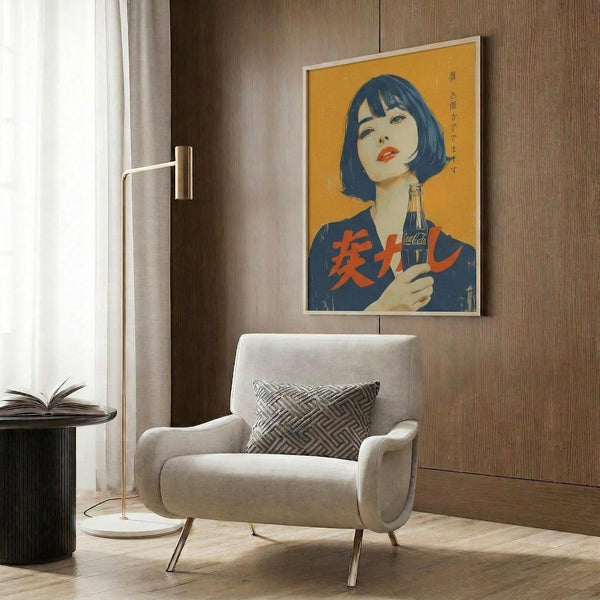 May include: Framed vintage-style Japanese Coca-Cola poster featuring woman with black bob haircut and red lips holding Coke bottle against yellow background with red Japanese text, displayed on wood-paneled wall above cream upholstered armchair with geometric throw pillow, brass floor lamp, and dark round side table with open book
