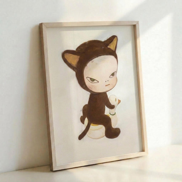 May include: Framed art print displayed against white wall showing stylized illustration of pale child character wearing brown cat costume with pointed ears, sitting on yellow duck float. Artwork features muted color palette with soft brushstroke style. Light wooden frame contains white matted print, leaning casually against wall surface with natural lighting creating gentle shadows.