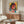 May include: Colorful cyberpunk-style portrait artwork displayed in thin frame above wooden sideboard in modern living room. The vibrant poster features a woman wearing headphones and sunglasses in pink, yellow, and blue tones with digital glitch effects. White curved chair and round glass coffee table are positioned nearby, with warm natural lighting illuminating the cream-colored walls.