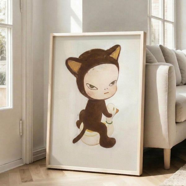 May include: Framed artwork displaying a whimsical illustration of a pale-faced child character wearing a brown cat costume with pointed ears, sitting on a yellow and white rubber duck. The artwork has soft, muted colors on cream background within a light wooden frame, positioned against white walls near large windows with a beige upholstered chair visible in a bright, minimalist living room setting.