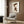 May include: Framed art print displaying a cute character in brown cat costume with orange ears sitting on white duck, hung on wood-paneled wall above modern beige armchair with geometric pillow. Room features brass floor lamp, dark round side table with open book, and neutral decor with warm lighting.