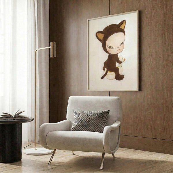 May include: Framed art print displaying a cute character in brown cat costume with orange ears sitting on white duck, hung on wood-paneled wall above modern beige armchair with geometric pillow. Room features brass floor lamp, dark round side table with open book, and neutral decor with warm lighting.