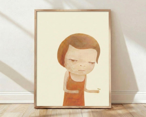May include: Framed artwork showing a child-like figure with brown bob haircut and closed eyes, wearing an orange sleeveless top, rendered in soft watercolor style against cream background. Natural wood frame sits on light wooden floor against white textured wall with gentle shadows.