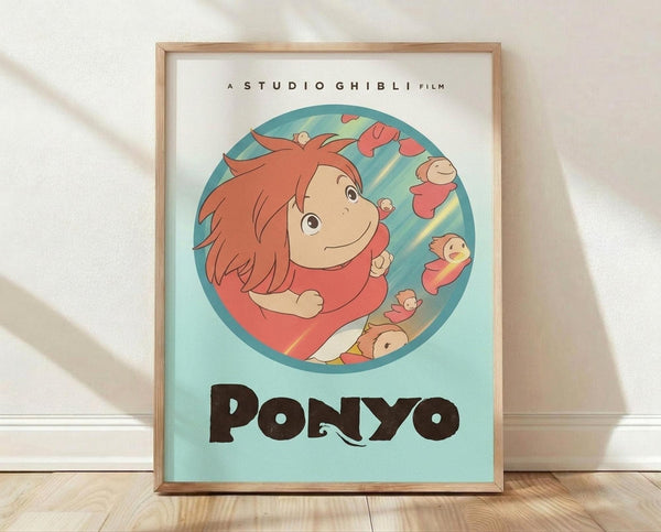 May include: Framed Studio Ghibli Ponyo poster print in light wood frame, leaning against white wall on wooden floor. Features circular illustration of red-haired girl Ponyo in coral dress floating underwater with goldfish, set against turquoise background. Bold black "PONYO" title below artwork with "A Studio Ghibli Film" text above. Minimalist room setting with soft natural lighting casting diagonal shadows on white textured wall.