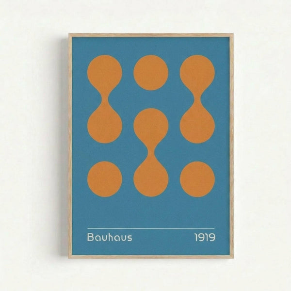 A minimalist poster with blue background featuring nine orange geometric shapes arranged in a 3x3 grid. The shapes include circles and hourglass or figure-eight forms. White text at bottom reads "Bauhaus 1919" with a thin horizontal line above. The artwork is displayed in a thin wooden frame against a white wall, showcasing clean geometric design principles.