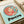 Light blue poster print featuring Ponyo, the red-haired girl character from Studio Ghibli, inside a circular frame surrounded by small floating figures. The character has orange-red hair and wears a red outfit. "PONYO" appears in large black letters at the bottom, with "STUDIO GHIBLI FILM" text at the top. The print sits on a cream-colored surface next to rolled white paper in soft, warm lighting.