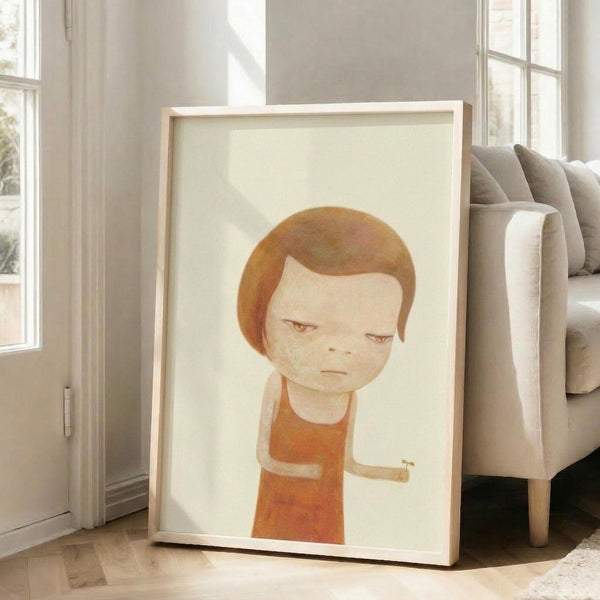 May include: Framed art print featuring a minimalist illustration of a child-like figure with reddish-brown hair wearing an orange sweater against a cream background, displayed in a bright living room next to a beige sectional sofa with natural light streaming through white-framed windows onto wooden floors.