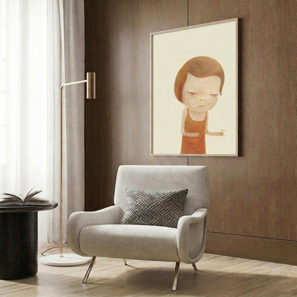 May include: Framed poster print featuring a stylized cartoon child with brown hair wearing an orange shirt, displayed on wood paneled wall above a beige upholstered armchair with geometric patterned pillow. Modern reading corner with brass floor lamp, dark side table with open book, and natural lighting from window with curtains.