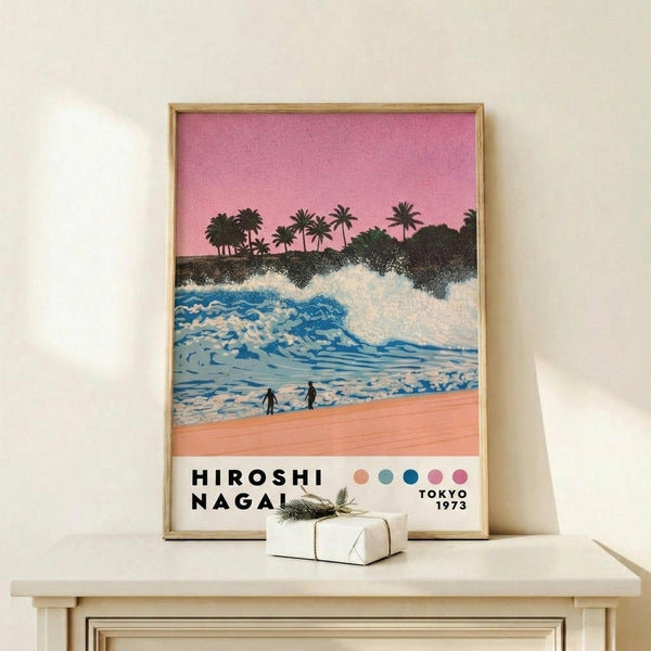May include: Framed poster print displayed on light wood shelf against cream wall. Artwork shows tropical beach scene with blue ocean waves, coral pink sand, silhouetted palm trees against pink sunset sky, and two small figures on shore. Text reads "HIROSHI NAGAI" and "TOKYO 1973" with colored dots below. Small wrapped gift box with evergreen sprig sits beside thin gold frame.