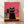May include: Framed poster print leaning against white wall on light wood floor with dramatic shadow. Features stylized illustration of black cat with yellow sunglasses and collar as main subject, surrounded by smaller cats in pink, teal, and black all wearing blue-green sunglasses. Vibrant coral pink background with yellow and orange brick ledge. Simple light wood frame, approximately 16x20 inches scale.