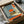 May include: Framed art print in cardboard shipping box with protective padding. Artwork shows Japanese-inspired scene with large red sun, silhouette of person sitting on hillside overlooking water, viewed through traditional sliding doors or window frame. Muted teal, orange, and cream color palette with geometric architectural elements and tatami mat flooring visible in foreground.