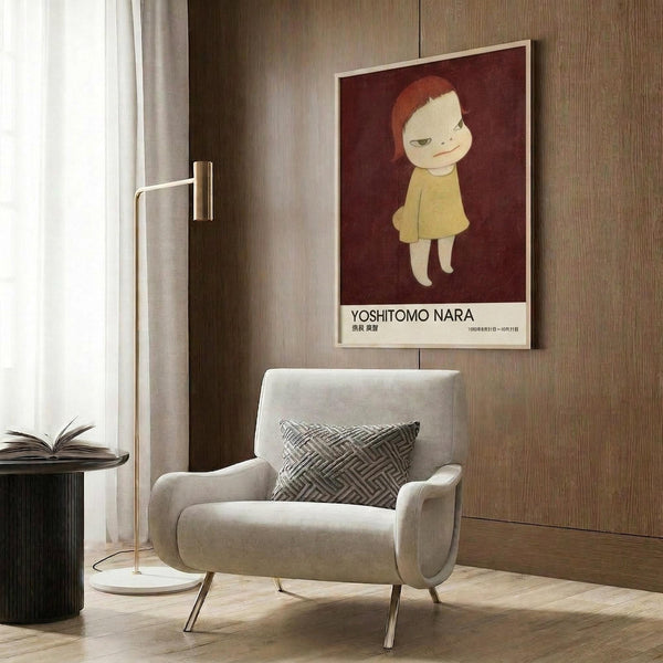 May include: Framed art poster featuring a stylized child character with red-orange hair wearing a yellow dress against a deep burgundy background, displayed on wood-paneled wall above a beige upholstered armchair with geometric patterned pillow, alongside a brass floor lamp and dark side table with open book in a modern living room setting with warm neutral tones.