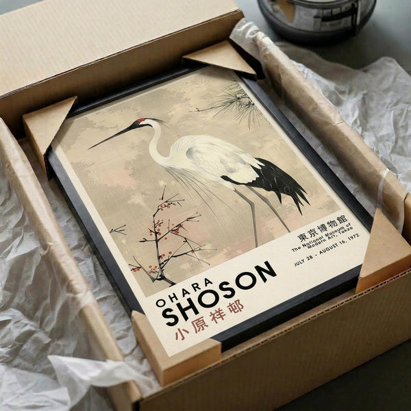 May include: Framed vintage Japanese-style poster featuring a white crane with black wing tips and red crown marking, standing among delicate flowering branches and pine needles on beige background. The artwork is displayed in a black frame inside an open cardboard shipping box with protective tissue paper, alongside wooden packaging tubes on a neutral surface.