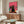 May include: A framed poster featuring a large black cat wearing yellow sunglasses and a collar, surrounded by smaller colorful cats in pink and teal also wearing sunglasses, all set against a bright pink background. The artwork is displayed above a mid-century modern walnut credenza in a minimalist living room with white walls, accompanied by a cream upholstered chair and glass coffee table.