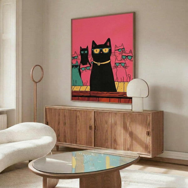 May include: A framed poster featuring a large black cat wearing yellow sunglasses and a collar, surrounded by smaller colorful cats in pink and teal also wearing sunglasses, all set against a bright pink background. The artwork is displayed above a mid-century modern walnut credenza in a minimalist living room with white walls, accompanied by a cream upholstered chair and glass coffee table.