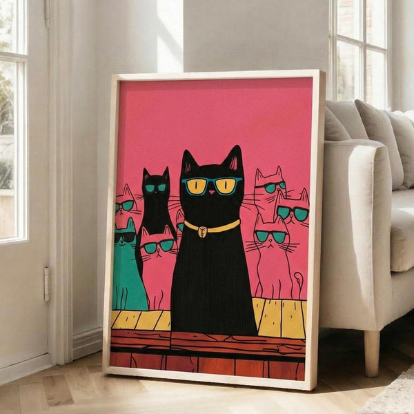 May include: Framed poster with pink background showing black cat wearing yellow sunglasses and collar in center, surrounded by colorful cats in teal sunglasses - some black, pink, and turquoise. Cats sit on yellow and orange wooden surface. White frame leans against beige wall next to gray sofa in bright living room with windows.