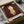 May include: Framed art print featuring a stylized illustration of a young girl with reddish-brown bob haircut and yellow dress against a deep burgundy background. The minimalist artwork shows Japanese aesthetic with clean lines and muted colors. Print is displayed in black frame within cardboard packaging surrounded by brown paper wrapping materials on white surface.