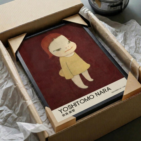May include: Framed art print featuring a stylized illustration of a young girl with reddish-brown bob haircut and yellow dress against a deep burgundy background. The minimalist artwork shows Japanese aesthetic with clean lines and muted colors. Print is displayed in black frame within cardboard packaging surrounded by brown paper wrapping materials on white surface.