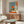 May include: Japanese-inspired poster with orange sun, figure by water, and Japanese text, displayed above wooden credenza in modern living room with white sculptural chair, brass floor lamp, glass coffee table, and neutral walls
