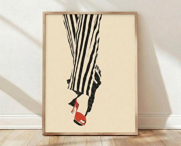 May include: Framed fashion illustration print leaning against white textured wall on light wood floor. Cream-colored poster shows black and white striped wide-leg pants with one foot wearing a red high heel sandal. Simple line art style in thin natural wood frame with subtle shadows cast on wall.