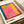 Colorful abstract art book or catalog cover featuring a vibrant rectangular composition with pink center, yellow and orange surrounding areas, and teal border. The cover displays "ROTHKO" in bold black letters at bottom with red circular accents, and "1903-1970 A RETROSPECTIVE" text in upper right corner. Book lies open on white surface showing textured, painterly brushwork in warm and cool tones.