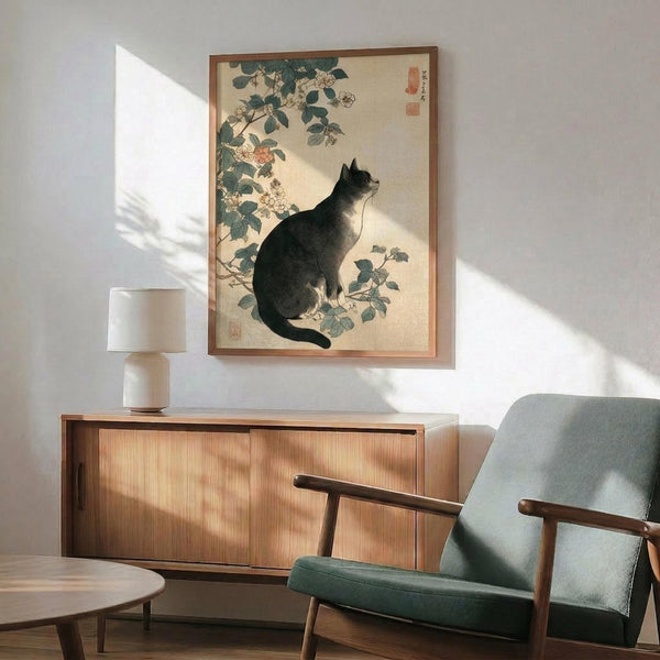 May include: Japanese woodblock print artwork featuring a black cat sitting among flowering rose branches, displayed in wooden frame above mid-century modern walnut credenza with ceramic table lamp, next to sage green upholstered armchair with wooden arms in bright sunlit room with white walls