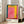 May include: A framed exhibition poster featuring an abstract painting with vibrant pink, yellow, orange and teal color blocks in Rothko's signature style. The white poster displays "ROTHKO" and "1903-1970 A RETROSPECTIVE" in dark text below the artwork. The thin wooden frame leans against a white wall next to a beige upholstered sofa in a bright, minimalist living room with large windows and natural light.