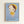 May include: Framed poster print mounted on white wall featuring stylized illustration of pale child-like figure with oversized head, green eyes, brown bob haircut with yellow beret. Character wears yellow dress with small flower detail, holds white object, stands against soft blue gradient background. Text reads "YOSHITOMO NARA" with Japanese characters and date "1992年8月31日〜10月31日" below. Natural wood frame surrounds blue-toned artwork in minimalist room setting.