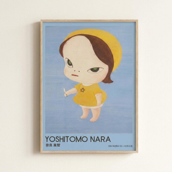 May include: Framed poster print mounted on white wall featuring stylized illustration of pale child-like figure with oversized head, green eyes, brown bob haircut with yellow beret. Character wears yellow dress with small flower detail, holds white object, stands against soft blue gradient background. Text reads "YOSHITOMO NARA" with Japanese characters and date "1992年8月31日〜10月31日" below. Natural wood frame surrounds blue-toned artwork in minimalist room setting.