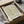 May include: Framed poster print featuring William Morris floral pattern in muted green, coral and cream tones displayed in cardboard shipping box with protective tissue paper wrapping and tape roll nearby on white fabric surface.
