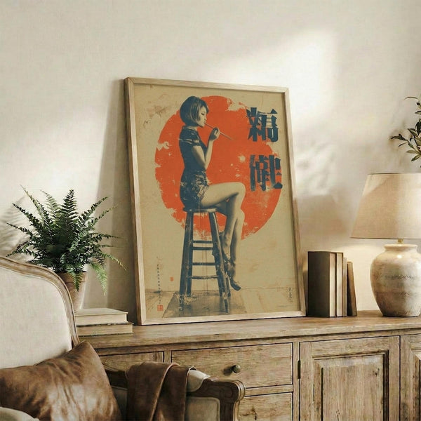 May include: Framed vintage-style poster featuring woman in dark blue cheongsam dress sitting on wooden stool against large red circular background with vertical Japanese characters, displayed on rustic wooden sideboard alongside fern plant, ceramic vase, and books in neutral-toned living room setting with beige armchair.