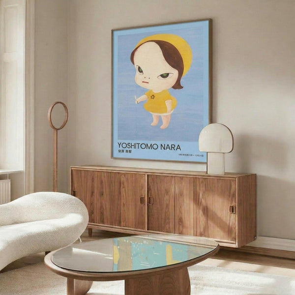 May include: Framed poster of stylized cartoon girl with brown hair, yellow dress and halo against blue background, displayed above wooden sideboard in modern living room with white curved chair, oval glass coffee table, and minimalist decor featuring warm wood tones and neutral colors.