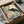 May include: Framed art print in black frame being carefully unpacked from cardboard box with protective wrapping. The artwork features an elegant black crane with red crown standing among pink peonies and green foliage in traditional Japanese artistic style. Warm beige and green tones throughout the botanical illustration, shown nestled in white tissue paper packaging.