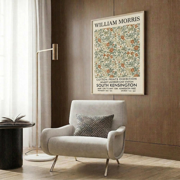 May include: Framed vintage floral poster with green foliage and orange flowers displayed on warm wood paneled wall above beige upholstered armchair with geometric patterned throw pillow. Modern brass floor lamp and round side table with open book complete the cozy reading nook scene with natural lighting from nearby window.