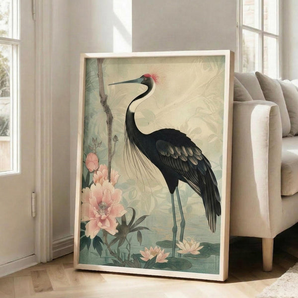 May include: Framed poster print displayed in bright living room featuring Japanese-style illustration of elegant black crane with red crown and long curved neck standing among pink peonies and lotus flowers on muted green background. Light wooden frame leans against white wall next to beige upholstered armchair near tall windows with natural sunlight streaming across hardwood floors.