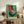 May include: Framed vintage-style poster with turquoise background featuring illustrated record player and Japanese text, displayed on rustic wooden sideboard alongside fern plant, ceramic vase, and stacked books in neutral-toned living room setting