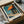 May include: Edward Hopper art print in cardboard box with protective wrapping. The poster shows a modernist building with orange triangular roof, teal walls, and large windows casting geometric shadows. Print appears medium-sized, nestled in brown packaging materials with rolled tubes nearby on white fabric surface.