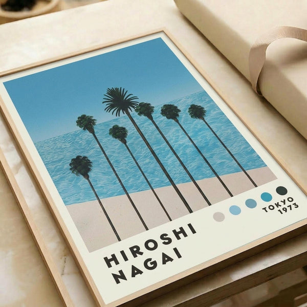 May include: Framed art print featuring stylized palm trees in silhouette against blue sky and ocean backdrop, displayed on light wooden surface next to beige fabric roll. The minimalist poster shows tall palm trees with long dark trunks and leafy crowns, rendered in muted tones of blue, beige, and green. Artist name and Tokyo 1973 text appear at bottom with small colored dots. Natural wood frame complements the coastal aesthetic.