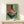 May include: Framed vintage-style poster with turquoise background featuring retro record player illustration in red and cream colors, displayed on light wood console table with small white wrapped gift, against white wall in minimalist room setting