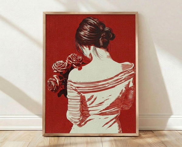 May include: Framed art print showing woman viewed from behind with dark hair in bun, holding red roses, wearing flowing white garment with red line details, set against deep red background. Natural wood frame displayed on light wooden floor against white wall with soft window light shadows.
