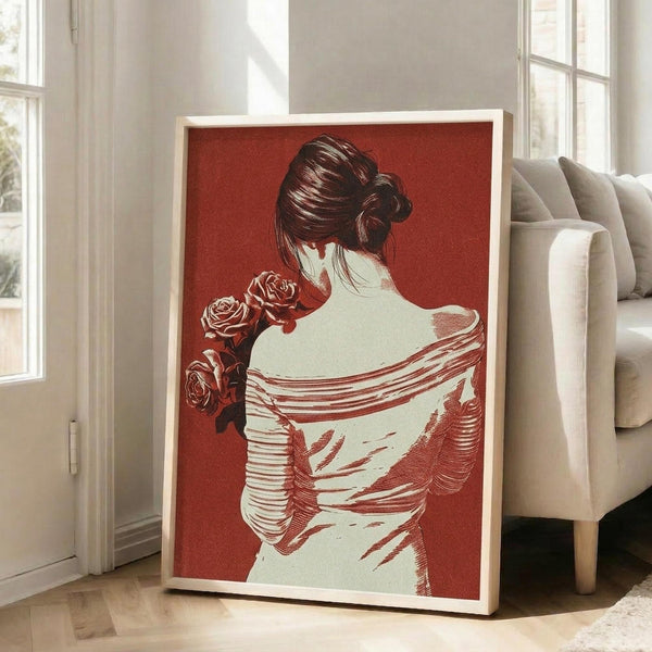 May include: Large framed poster with red background showing back view of woman with hair in bun holding roses, displayed in bright living room next to beige sofa. Artwork features vintage-style illustration in red and cream tones with light wood frame, leaning against white wall near windows.