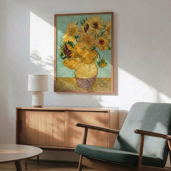 May include: Van Gogh's Sunflowers painting reproduction in wooden frame hanging above mid-century modern wooden sideboard with table lamp. Teal upholstered armchair with wooden arms sits nearby. Bright sunlight casts dramatic shadows across white wall. The artwork shows yellow sunflowers in ceramic vase against turquoise background.
