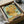 Framed reproduction of Van Gogh's sunflowers painting being unboxed from cardboard packaging with protective tissue paper. The artwork shows vibrant yellow sunflowers in a ceramic vase against a turquoise background, displayed in a black frame. Wooden packaging materials and bubble wrap are visible around the unboxing scene on a neutral surface.