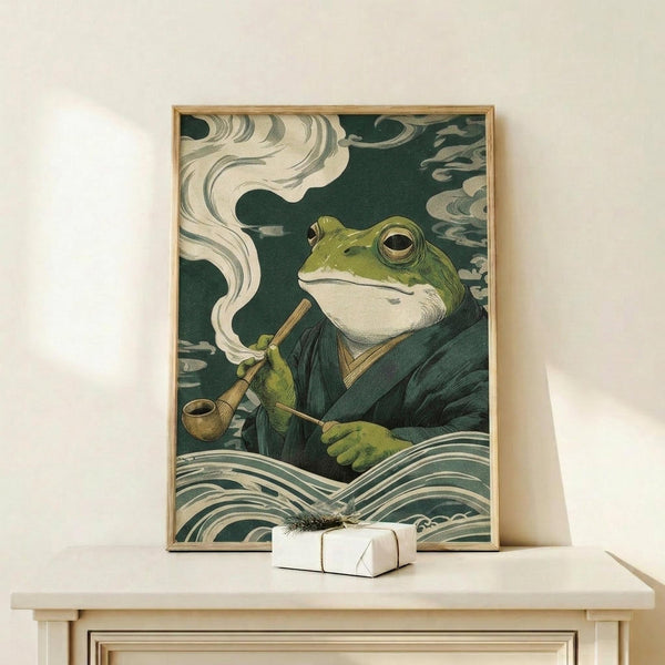 May include: Framed poster print displayed on light wood console table against white wall. Artwork shows anthropomorphic green frog wearing dark robes, smoking wooden pipe with white smoke swirls, surrounded by stylized ocean waves in traditional Japanese ukiyo-e woodblock print style. Teal and cream color palette with intricate wave patterns. Small wrapped gift box sits beside frame.