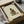 May include: Framed art print showing woman in green striped robe reading book while sitting cross-legged on neutral beige background, displayed in black frame being unpacked from cardboard shipping box with protective wrapping and packing materials on white surface