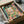 May include: Framed Henri Matisse painting print being carefully unpacked from brown cardboard shipping box with protective tissue paper. The artwork shows a vibrant interior scene with an open window overlooking boats on water, featuring bold brushstrokes in pink, green, orange and blue Fauvist colors. Black frame sits nestled in white tissue paper with wooden dowels visible for protection during shipping.