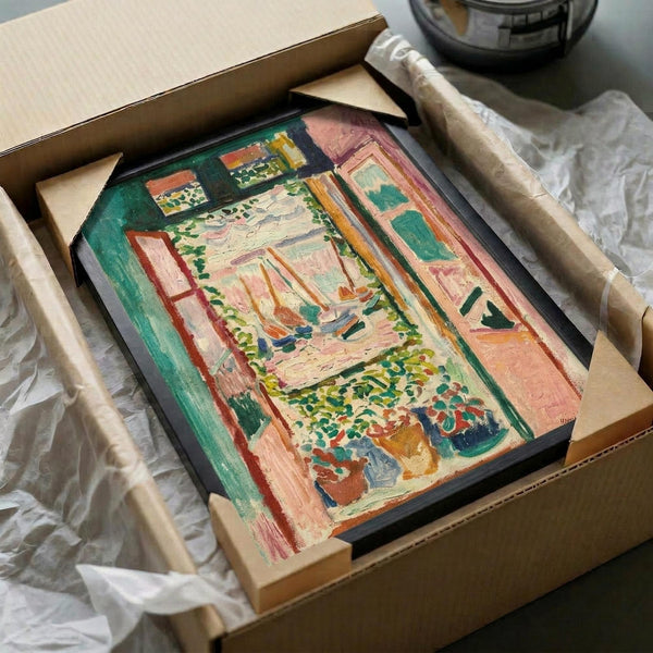 May include: Framed Henri Matisse painting print being carefully unpacked from brown cardboard shipping box with protective tissue paper. The artwork shows a vibrant interior scene with an open window overlooking boats on water, featuring bold brushstrokes in pink, green, orange and blue Fauvist colors. Black frame sits nestled in white tissue paper with wooden dowels visible for protection during shipping.