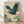 May include: Framed Japanese-style artwork featuring a blue-green heron with outstretched wings flying through swirling cream and teal clouds. The print has a vintage woodblock aesthetic with detailed feathers and decorative cloud patterns. Japanese characters appear in the upper left corner with a red seal stamp. The artwork is displayed in a light wood frame, leaning against a white wall on light wooden flooring with natural shadows casting across the scene.