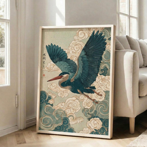 May include: Framed Japanese-style artwork of a blue-gray heron in flight with outstretched wings against swirling clouds and traditional wave patterns in teal and cream colors. The print features Japanese calligraphy in the upper left corner and sits propped against a white wall next to a beige upholstered chair in a bright, modern living room with large windows.